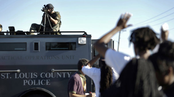 A member of the St. Louis County Police Department points his weapon in the direction of a group of protesters in Ferguson, Mo., on August 10, 2014. | Jeff Roberson / AP