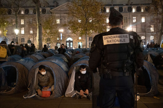 A police officer stands in front of migrants in a makeshift camp set up Nov. 23, 2020, on Place de la Republique in Paris. Paris police were filmed tossing migrants out of tents while evacuating the camp in the French capital. Their action came amidst protests against a new bill prohibiting citizens from filming the police. | Alexandra Henry / Utopia56 via AP