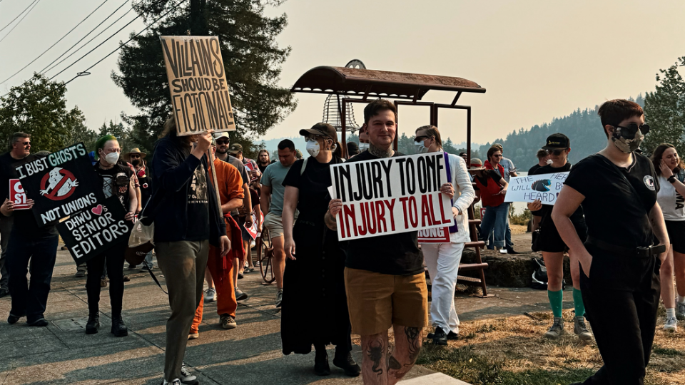 Supporters of DHWU showing off their union T-shirts and signs reading: I bust ghosts, not unions! DHWU loves Senior Editors! Villains should be fictional! Injury to one, Injury to all!